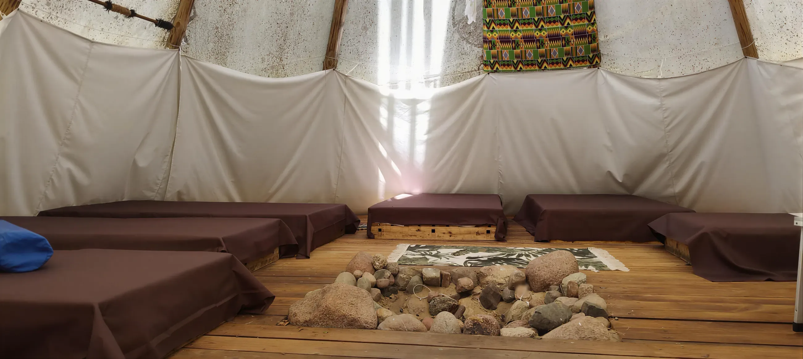 Wnętrze tipi: jasne płótno, drewniana podłoga i kamienny krąg na środku